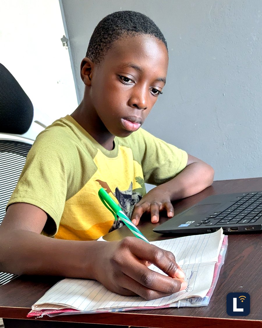 A Lory Online School student writing in a notebook next to a laptop